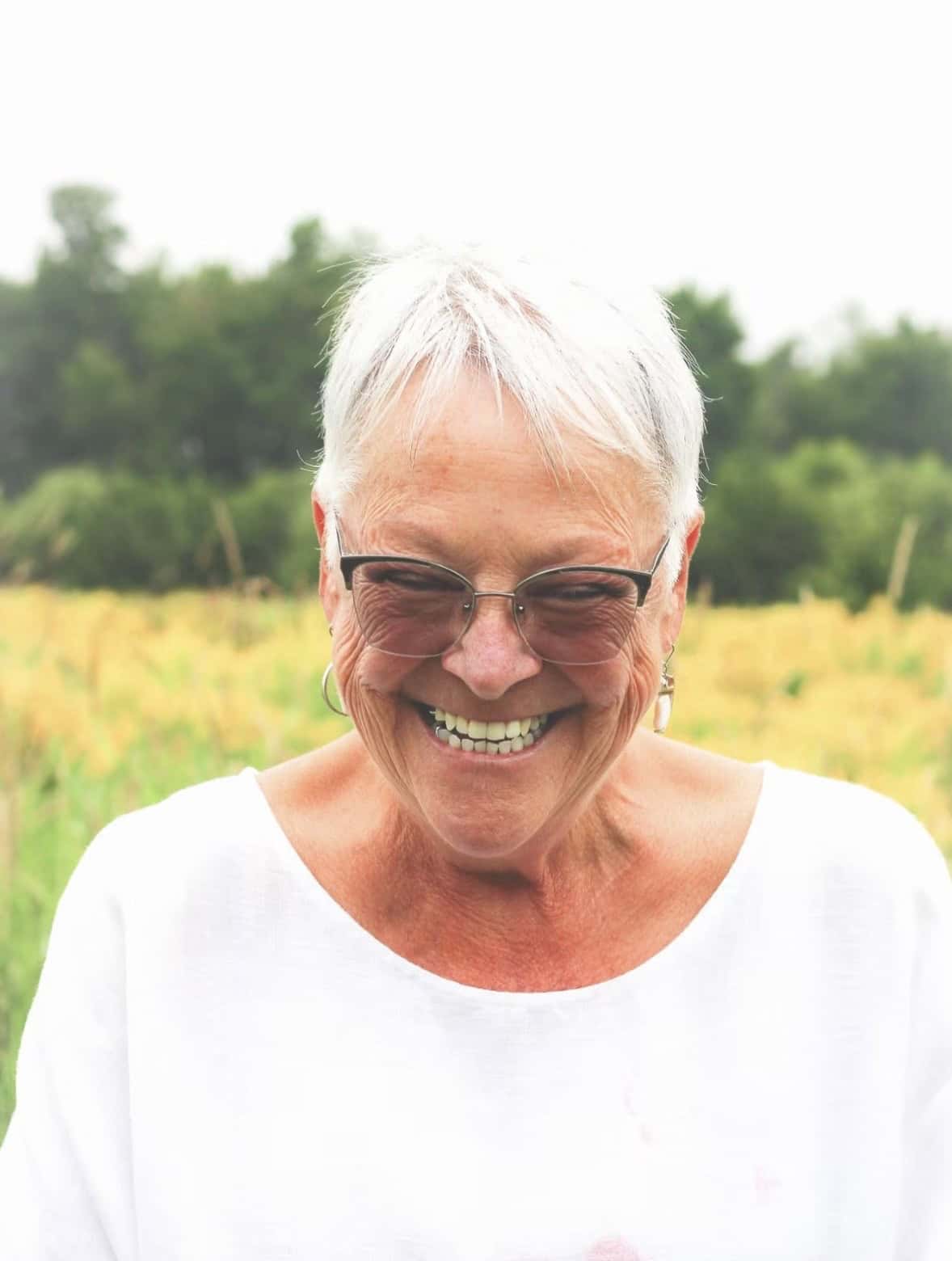 Sourire d'une femme âgée avec lunettes dans un champ vert.