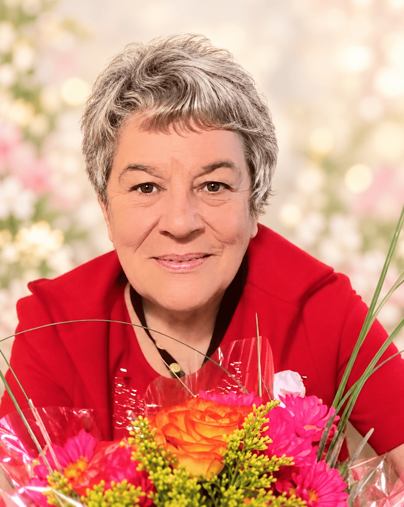 Portrait d'une femme âgée souriante avec fleurs colorées en arrière-plan.
