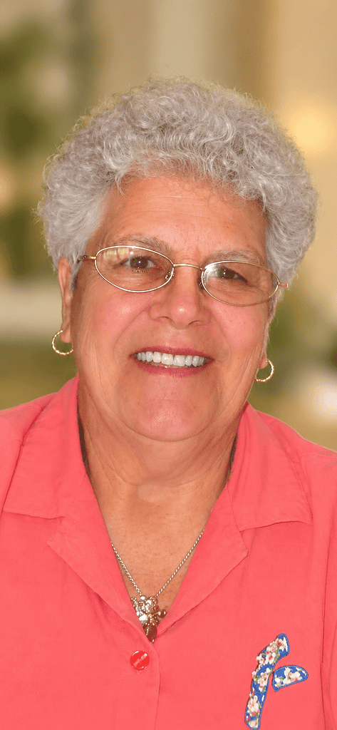 Portrait d'une femme âgée souriante portant des lunettes et une chemise rose.